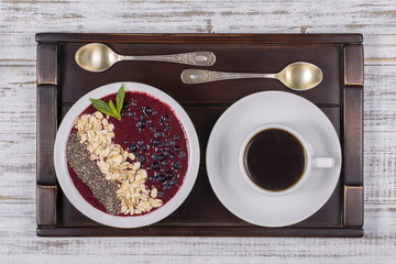 Cup of coffee and muesli made from blueberry, chia seeds, oat flakes with yogurt on a tray on white wooden table. Lifestyle concept. Close up, top view