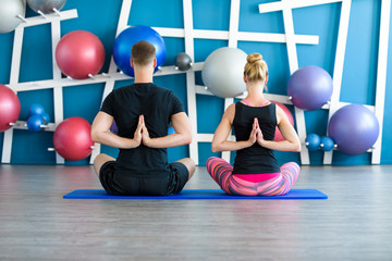 Fototapeta na wymiar Nice couple doing yoga in a studio. Young people in yoga class in Reverse Prayer Pose. Yoga group concept