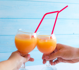 Palms holding glasses with orange cocktails on a blue background