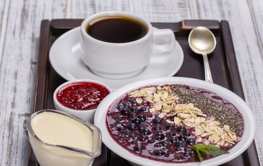 Cup of coffee and muesli made from blueberry, chia seeds, oat flakes with yogurt on a tray on white wooden table. Lifestyle concept. Close up, top view