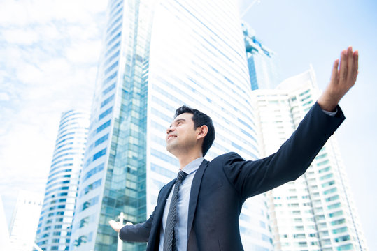 Businessman raising his arms opening palms with face looking up, in office building background