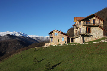 Fototapeta na wymiar two stone houses on the hill on the background of snowy mountains, clear blue sky, horizontal