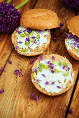 Toasted bread bruschetta with cream cheese and garlic edible flowers on olive wooden cutting board on stone slate gray background. Top view