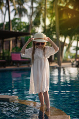 Beautiful cute girl in a hat near the pool at sunset. Paradise