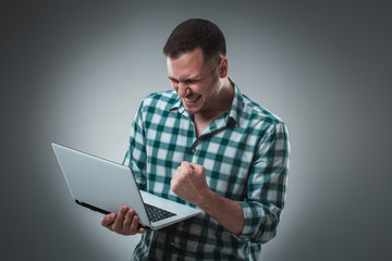 Attractive business man model in green shirt isolated on gray working with laptop, showing something by left hand.