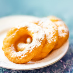 Fresh donuts topped with white sugar powder on a plate on colorful background close up. Russian traditional donuts