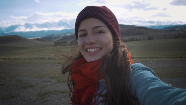 Young beautiful girl - hipster. He travels in the mountains. Calls to parents or friends on video communication. Sends greetings! Pleased with life and happy.