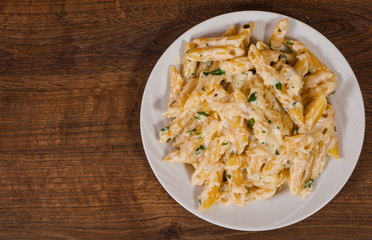 Penne pasta with cream sauce on wooden table with copy space. top view