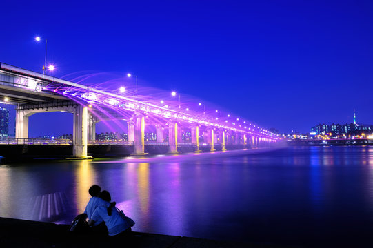 Couple love sitting at banpo bridge looking rainbow fountain show at night in Seoul, Soth Korea. 