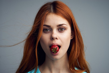 A woman holding a strawberry in her mouth, a strawberry sweet on a gray background