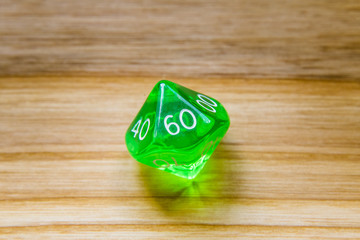 A translucent green ten sided playing dice on a wooden background with number sixty on a top
