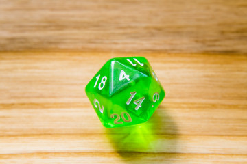 A translucent green twenty sided playing dice on a wooden background with number four on a top