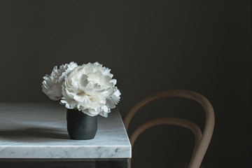 white peonies on marble table with wooden chair