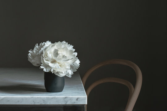 White peonies on marble table with wooden chair