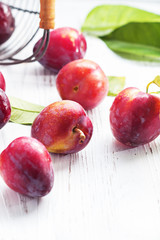Red plum fruits with green leaves on white background.