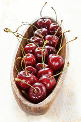 Ripe red cherries with water drops in a wooden elongated plate on an old painted table close up