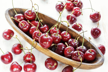 Ripe red cherries with water drops in a wooden elongated plate on an old painted table close up