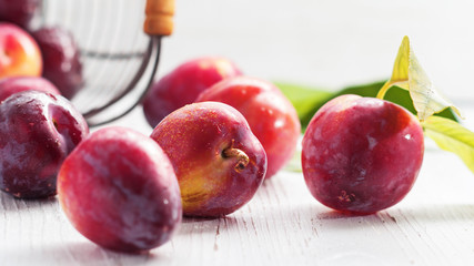 Red plum fruits with green leaves on white background.