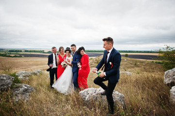 Groomsman or best man opening up the bottle of champagne in the countryside with wedding couple and braidsmaids with groomsman standing in the background.