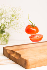 Sliced whole tomato flying above a wooden chopping board