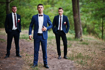 Handsome groom with cool groomsmen walking in the forest and having fun on a wedding day.