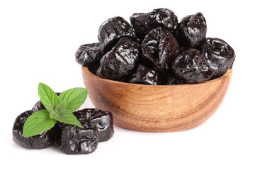 Dried plums or prunes with a mint leaf in wooden bowl isolated on white background