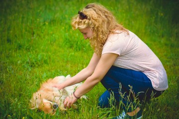 A woman is playing on the lawn with her best dog friend the red Pekingese