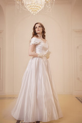 bride in wedding dress and white gloves in bright room with large chandelier