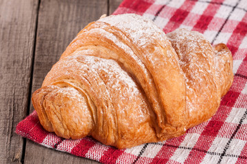 One croissant sprinkled with powdered sugar on a wooden table with napkin
