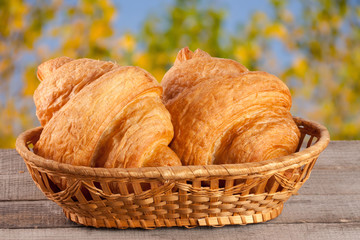 two croissant in a wicker basket on a wooden board with a blurry garden background