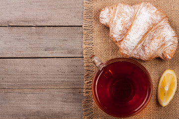 croissant with a cup of tea on an old wooden background with copy space for your text. Top view