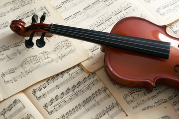 Close-up photo of vintage violin with bow and musical notes. Cello or fiddle and fiddlestick on ancient music sheet, rusted old yellow paper, sheet of music.