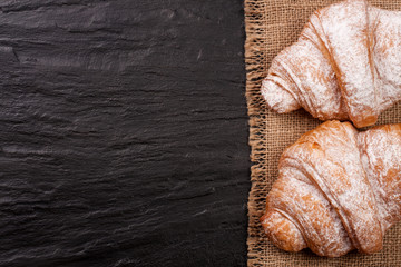 two croissant sprinkled with powdered sugar on black stone background with copy space for your text. Top view
