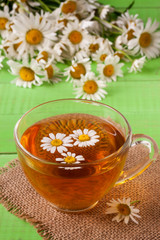 Herbal tea with fresh chamomile flowers on green wooden background