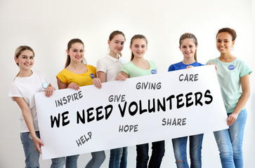 Group of teens holding poster with text WE NEED VOLUNTEERS on color background