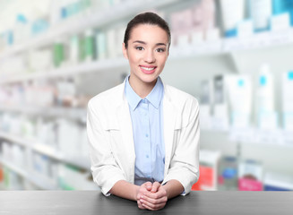 Young woman pharmacist standing at table on white background