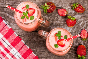 Glass of strawberry yogurt or smoothie with mint leaves on old wooden background. Top view