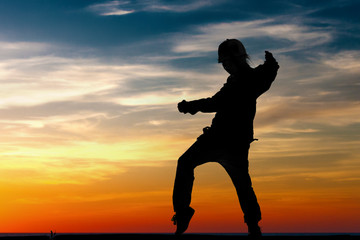 Silhouette of little girl dancing on sunset background. Summer child.