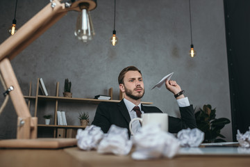 young businessman throwing paper airplane while sitting at workplace