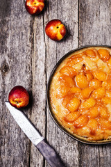 Tarte tatin upside down peach tart on vintage rustic wooden table. Summer baking. French cuisine. Selective focus. Toned image 