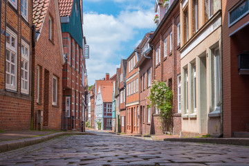 low angle shot of narrow cobblestone street with traditional half-timbered houses under blue summer sky in Stade, Germany