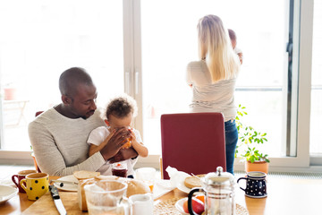 Young interracial family with little children having breakfast.