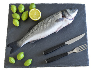 One ready to cook raw fish with fork, knife and lemon on stone slate board. With copy space.