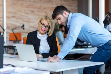 Colleagues chatting, sitting together at office table, smiling