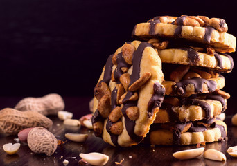 Cookies with peanuts, covered with chocolate icing, on a dark wooden background with space for text.