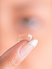 Young woman putting contact lens in her eye.