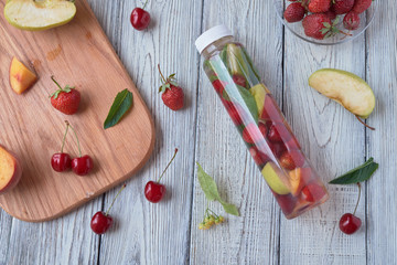 Fresh fruit detox water. Apple, cherry, peach, strawberry wooden table.