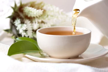 Photo sur Plexiglas Theé Gros plan versant du thé noir chaud dans une tasse de thé blanc, concept de temps de cérémonie du thé