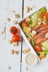 Caesar salad with fish in box on wooden surface