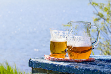 Jug and mug of beer on the table by the lake